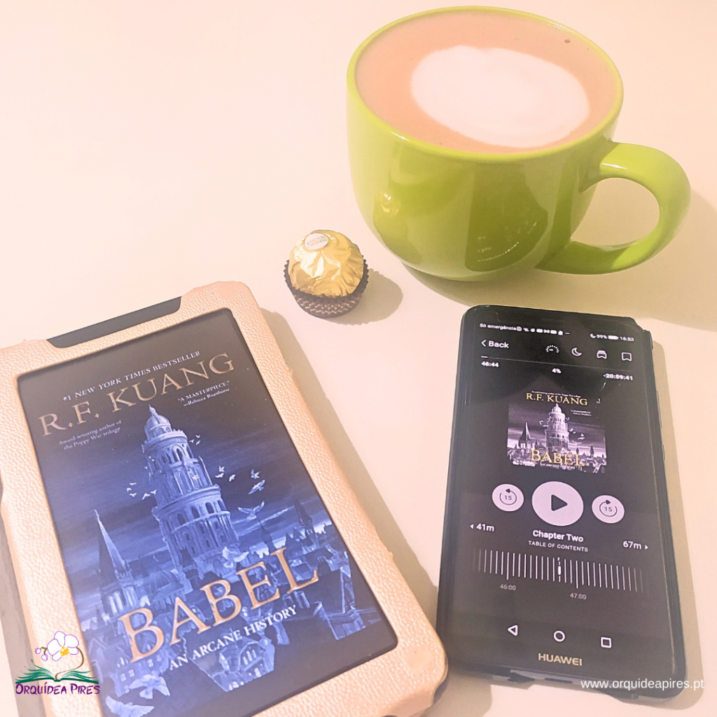 Babel, de R. F. Kuang, aberto num e-reader ao lado de um telemóvel com o audiobook do livro, numa sessão de leitura imersiva.